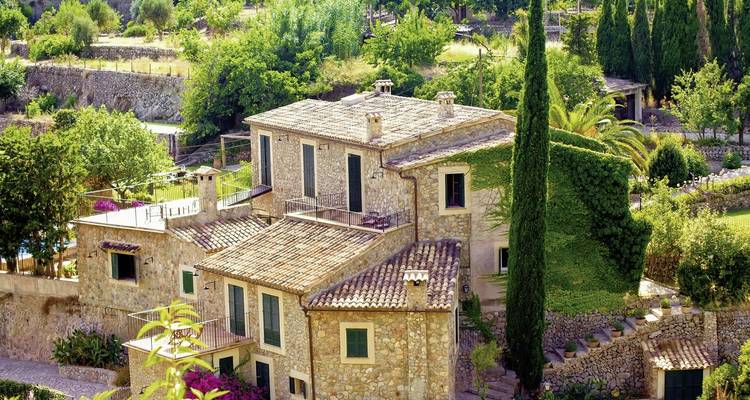 A stone house surrounded by lush gardens and trees.