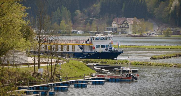 A cruise ship docked by a scenic riverside with surrounding greenery.