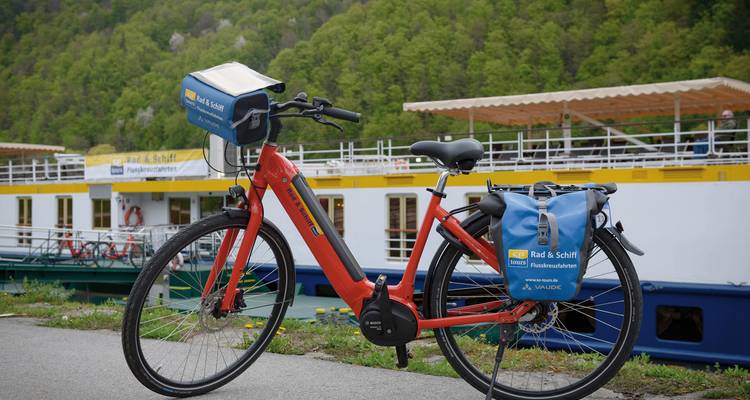 A red bicycle parked alongside a tour boat at a dock.
