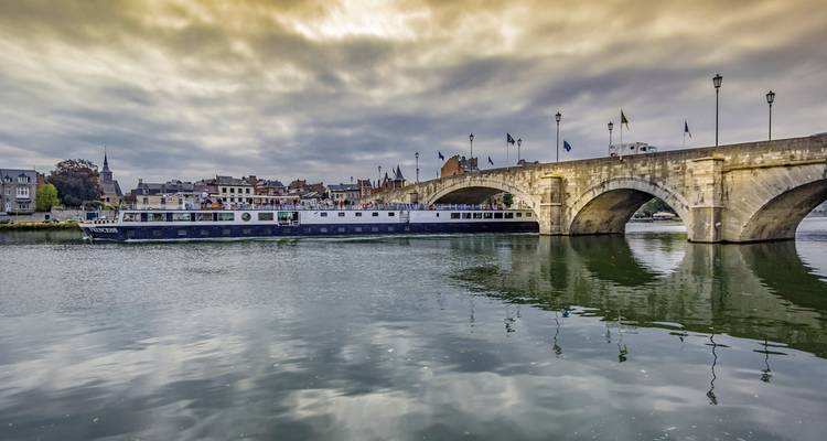 Riviercruiseboot nabij een oude stenen brug met een stadsdecor.