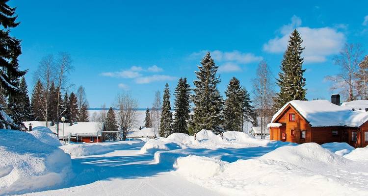 Un village enneigé avec des maisons en bois sous un ciel lumineux.