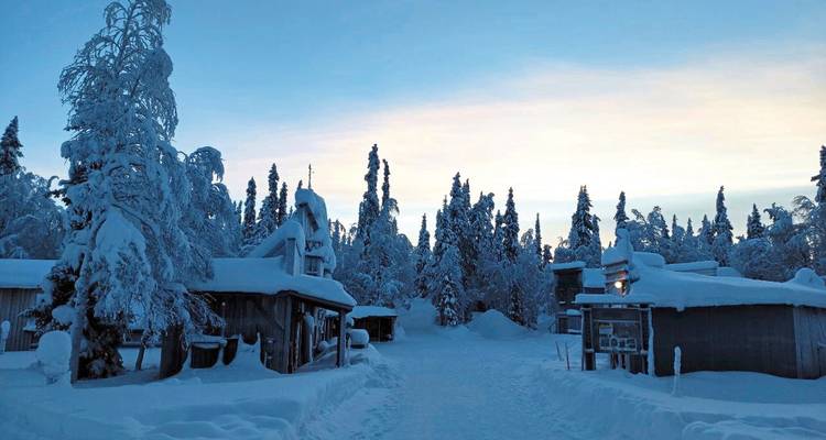 Snow-covered landscape with small wooden cottages surrounded by snow-laden trees.