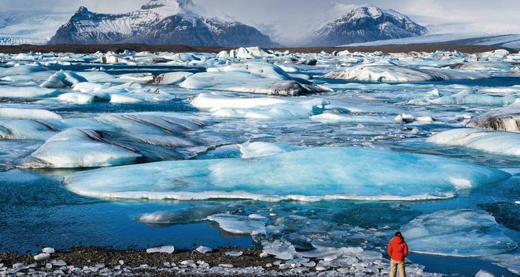 Eine Person, die eine gefrorene Lagune mit Gletschern und Eisbergen bewundert.