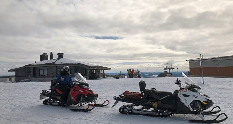 Motoneiges garées sur une plaine enneigée avec un bâtiment en arrière-plan.
