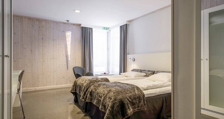 Intérieur d'une chambre d'hôtel moderne avec lits doubles et grandes fenêtres.