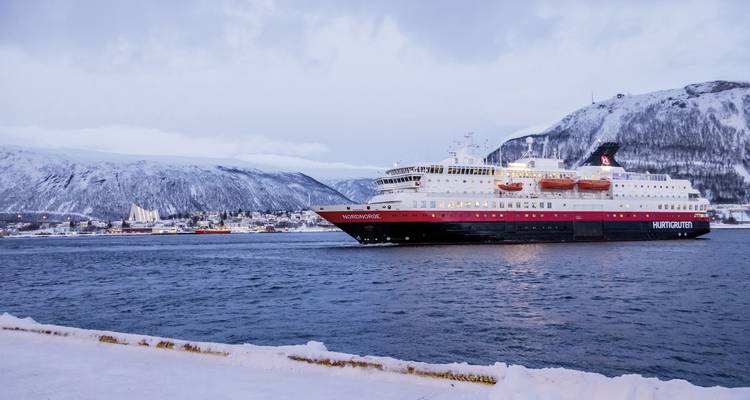 Navire de croisière naviguant sur les eaux glacées avec des montagnes enneigées en arrière-plan.