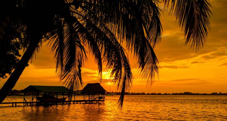 Coucher de soleil tropical sur un lac avec des palmiers et des huttes.