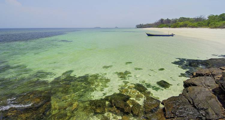Une plage sereine avec une eau claire et un petit bateau ancré près du rivage.