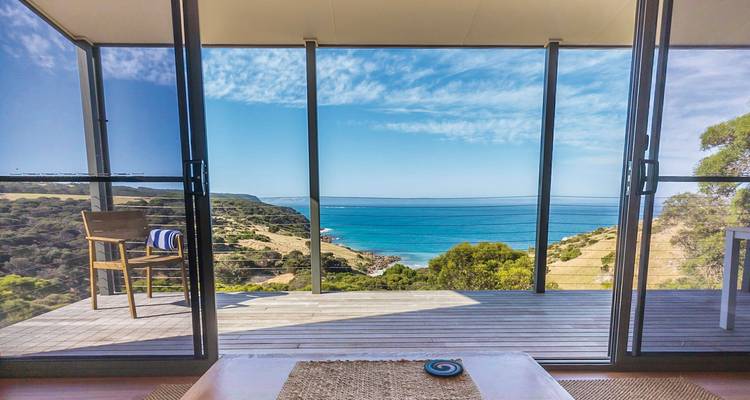 Vue depuis une fenêtre en verre d'une terrasse surplombant l'océan.