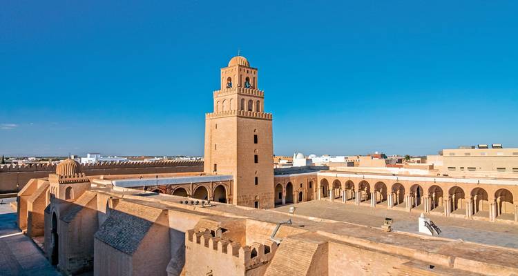 A large mosque courtyard with a prominent minaret under a clear sky.