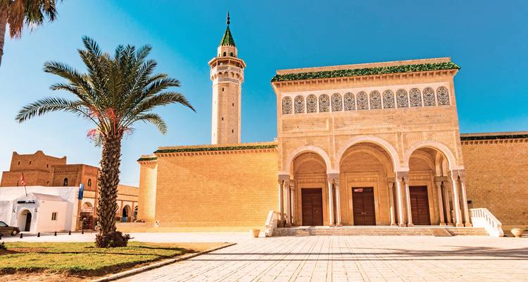 Mosquée ornée avec un grand minaret contre un ciel bleu clair.