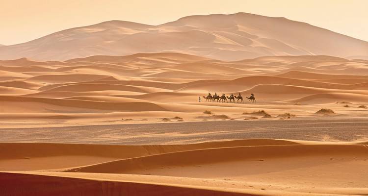 Eine Karawane von Kamelen mit Reitern, die Sanddünen in der Wüste durchquert.