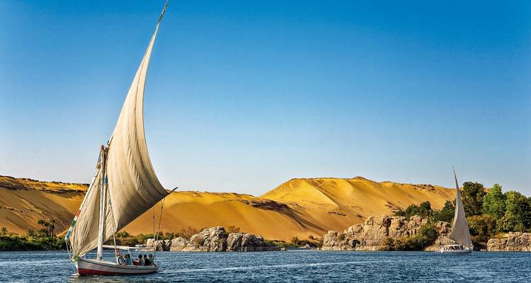 Traditional sailboat on a river with desert landscape in the background.