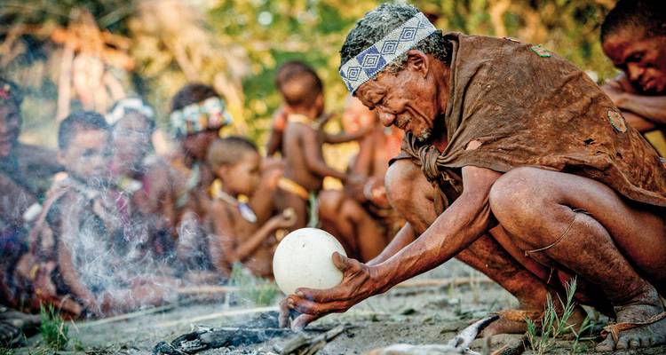 Des peuples autochtones assis autour d'un feu en tenue traditionnelle.