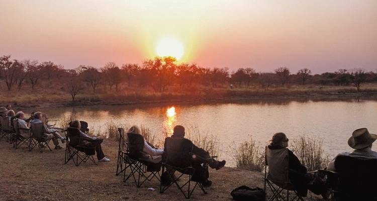 Des gens regardant le coucher de soleil au-dessus d'un plan d'eau assis sur des chaises.