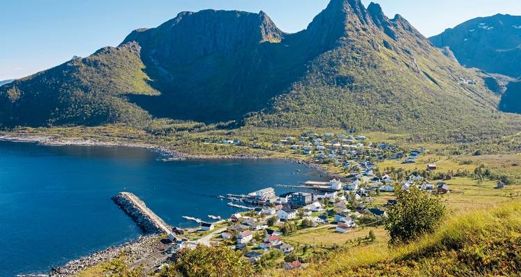 Coastal village with mountains and a harbor, viewed from a high vantage point.