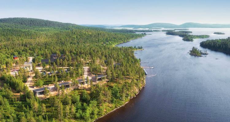 Luftaufnahme eines bewaldeten Gebiets mit einem See und Hütten.