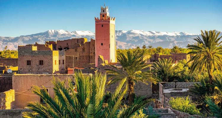 Traditionelles marokkanisches Gebäude mit Palmen vor schneebedeckten Bergen.