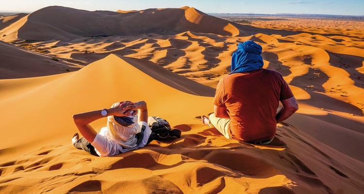 Zwei Menschen entspannen auf Sanddünen in der Wüste.