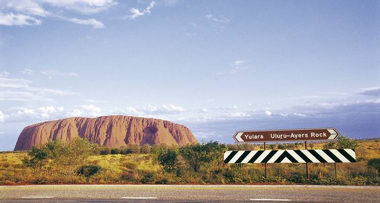 Vue d'Uluru avec des panneaux routiers au premier plan.