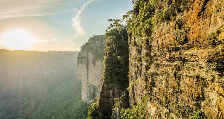 Vue spectaculaire de falaise avec rayons de soleil et vallée verdoyante en contrebas.