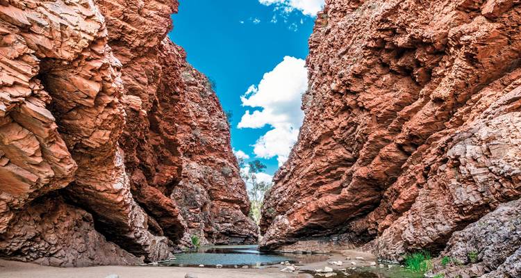 A canyon with clear blue sky overhead and a small body of water surrounded by rocky formations.