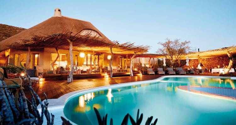 Luxurious pool area with thatched roofs and warm lighting at dusk.