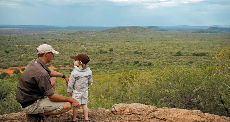 Ein Vater und Kind blicken über die weite Savannenlandschaft.