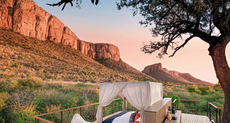 Ein luxuriöses Außenbett mit Blick auf felsige Hügel und Sonnenuntergang.