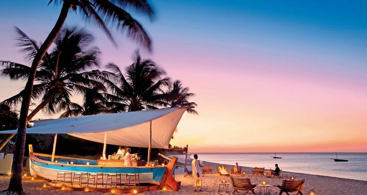 Beach bar scene at sunset with palm trees and people relaxing.