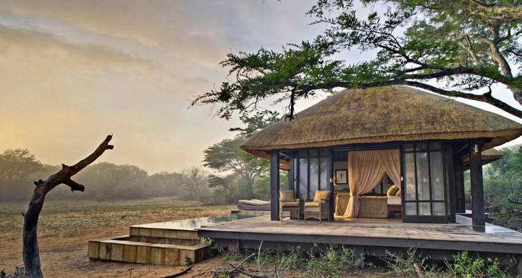 Thatched roof lodge in a natural setting with dusk light.