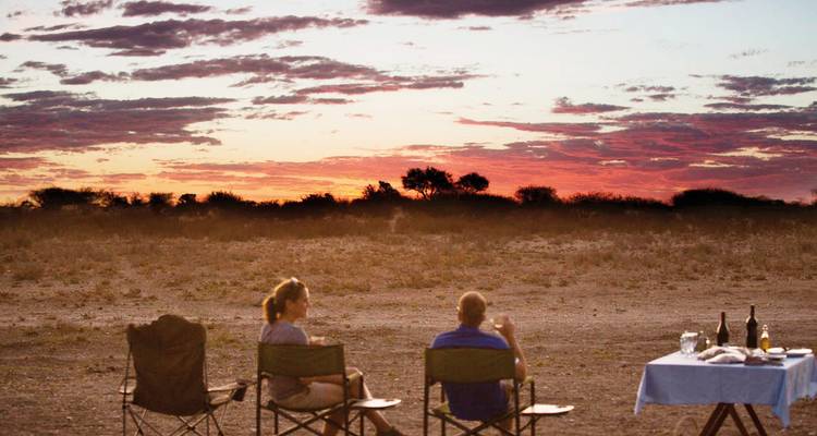 Couple enjoying drinks at sunset in a natural setting.