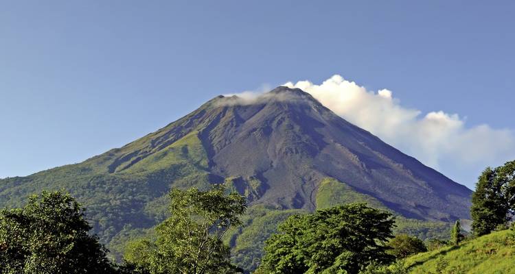 Volcano with plume of smoke and green hills in the foreground.