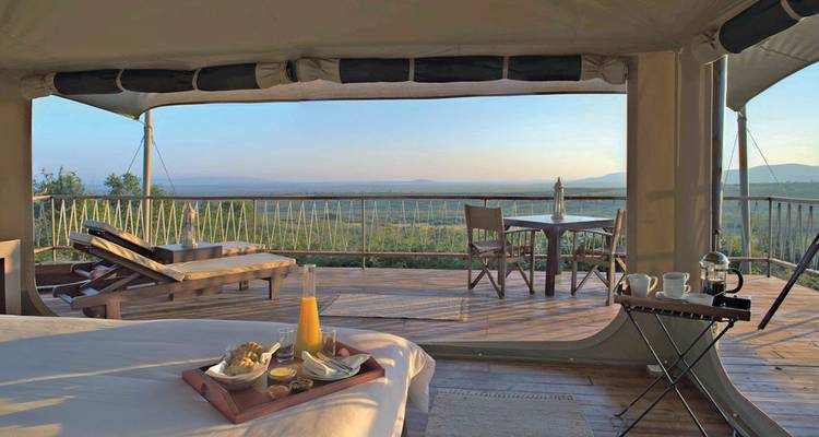 Blick aus einem Luxuszelt mit Bett und Balkon mit Aussicht auf die Landschaft.