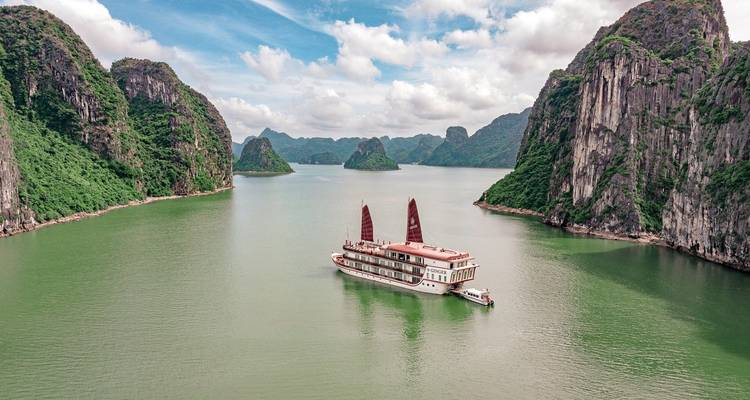 A cruise ship sailing in a bay surrounded by limestone cliffs.