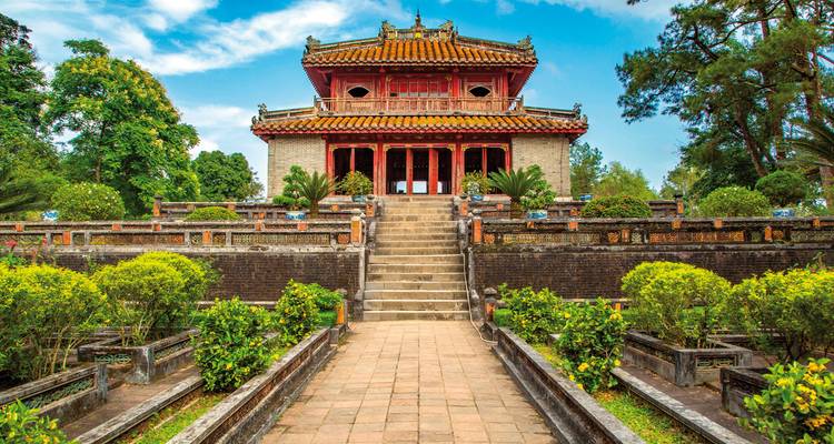 A historic temple with steps leading up to it and lush greenery.
