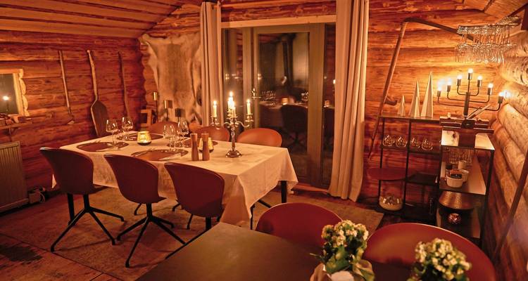 Gemütlicher Essbereich in einer Holzhütte, beleuchtet von Kerzenlicht.