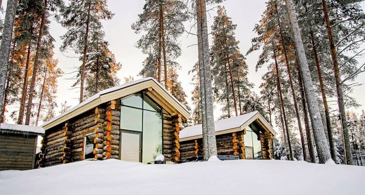 Holzhütten in einem verschneiten Wald mit hohen Bäumen.