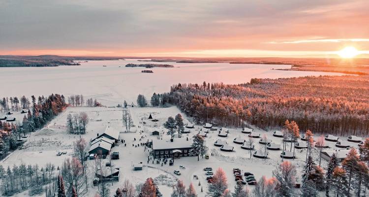 Luftaufnahme einer verschneiten Landschaft mit einem Sonnenuntergang im Hintergrund.