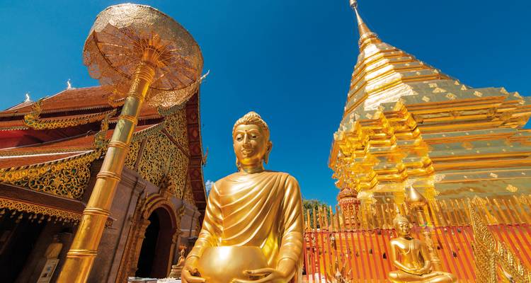 Statue dorée de Bouddha et un stupa sous un ciel bleu clair.