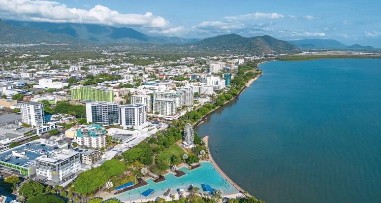 Coastal cityscape with beachfront, mountains, and blue sky.