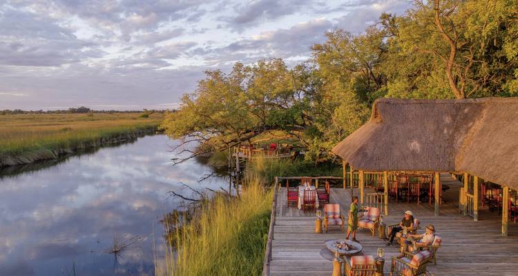 Scenic view of a riverside lodge with people sitting on a deck.