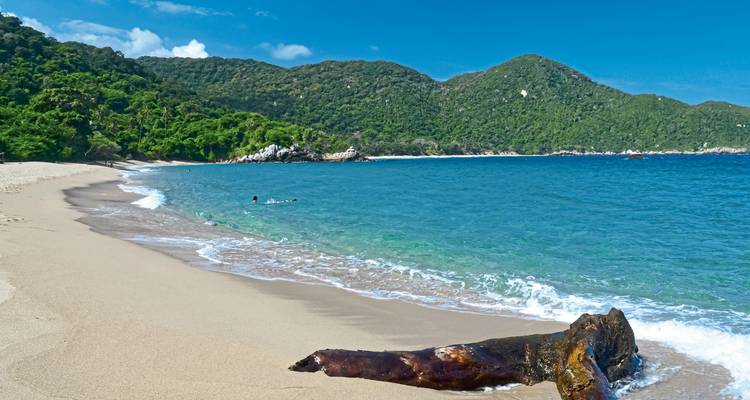 Beach with clear blue waters and lush green hills.