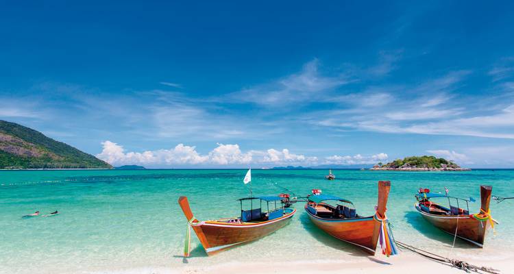 Trois bateaux sur une plage tropicale tranquille avec un ciel bleu.