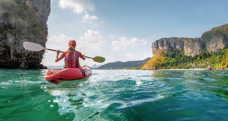Personne faisant du kayak sur des eaux turquoise près de falaises.