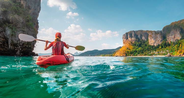 Kajakfahrer paddelt durch türkisfarbenes tropisches Wasser zwischen hoch aufragenden Kalksteinfelsen in Thailand.