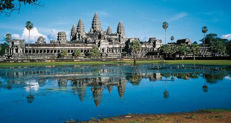 Complejo del templo de Angkor Wat reflejado en un lago tranquilo bajo un cielo azul.