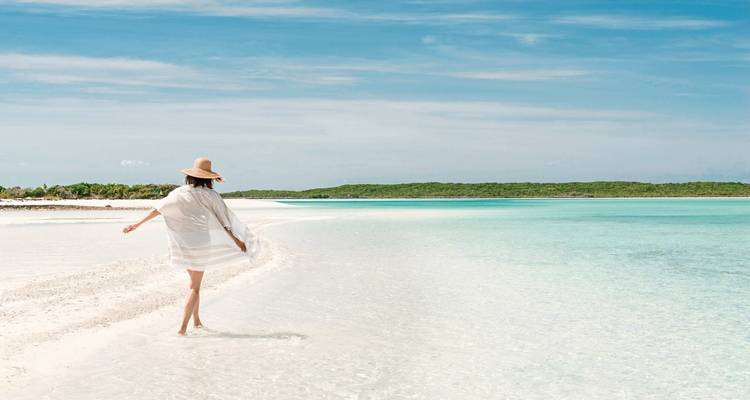A woman walking along a pristine white sand beach with turquoise water.