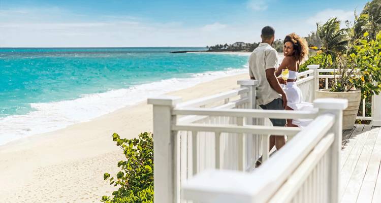 A couple standing on a balcony overlooking the ocean.