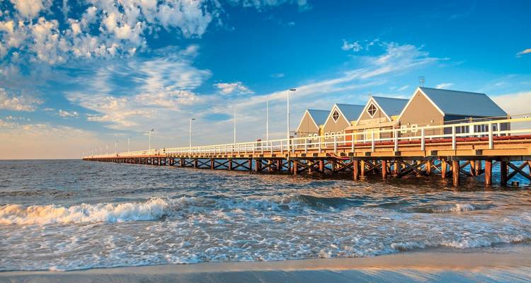 Pier, der sich in den Ozean erstreckt mit kleinen Häusern und einem Sonnenuntergangshimmel.